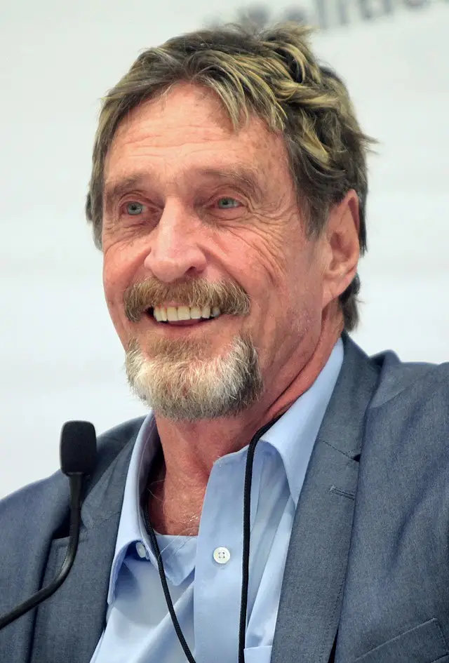 A close-up photo of actor John Hurt smiling broadly, wearing a grey suit jacket over a light blue collared shirt with a…
