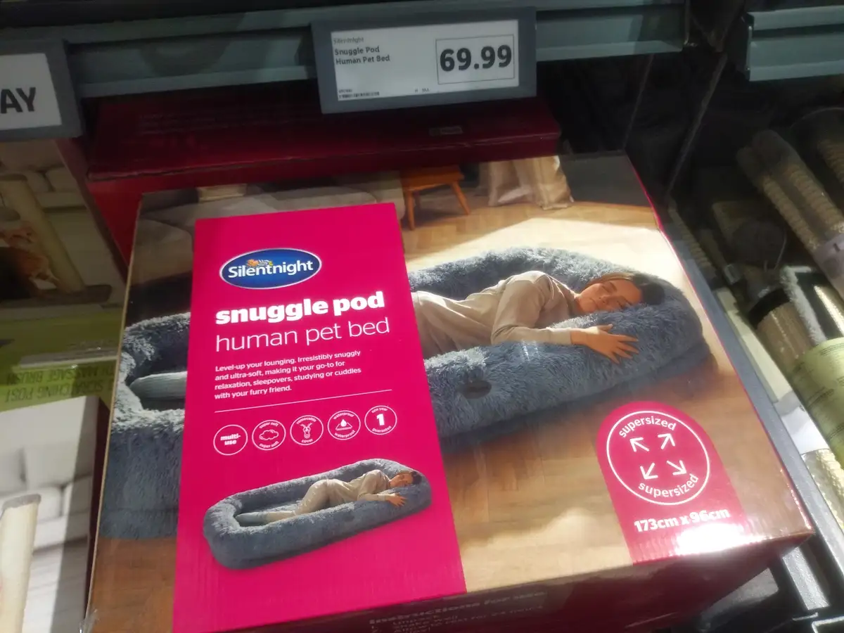A product box for a 'Silentnight Snuggle Pod Human Pet Bed' is displayed in a store, featuring an image of a person sleeping…