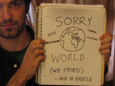 A man holds up a spiral-bound notebook with a hand-drawn globe and text. The globe is labeled with 'DÉSOLÉ' (French for…