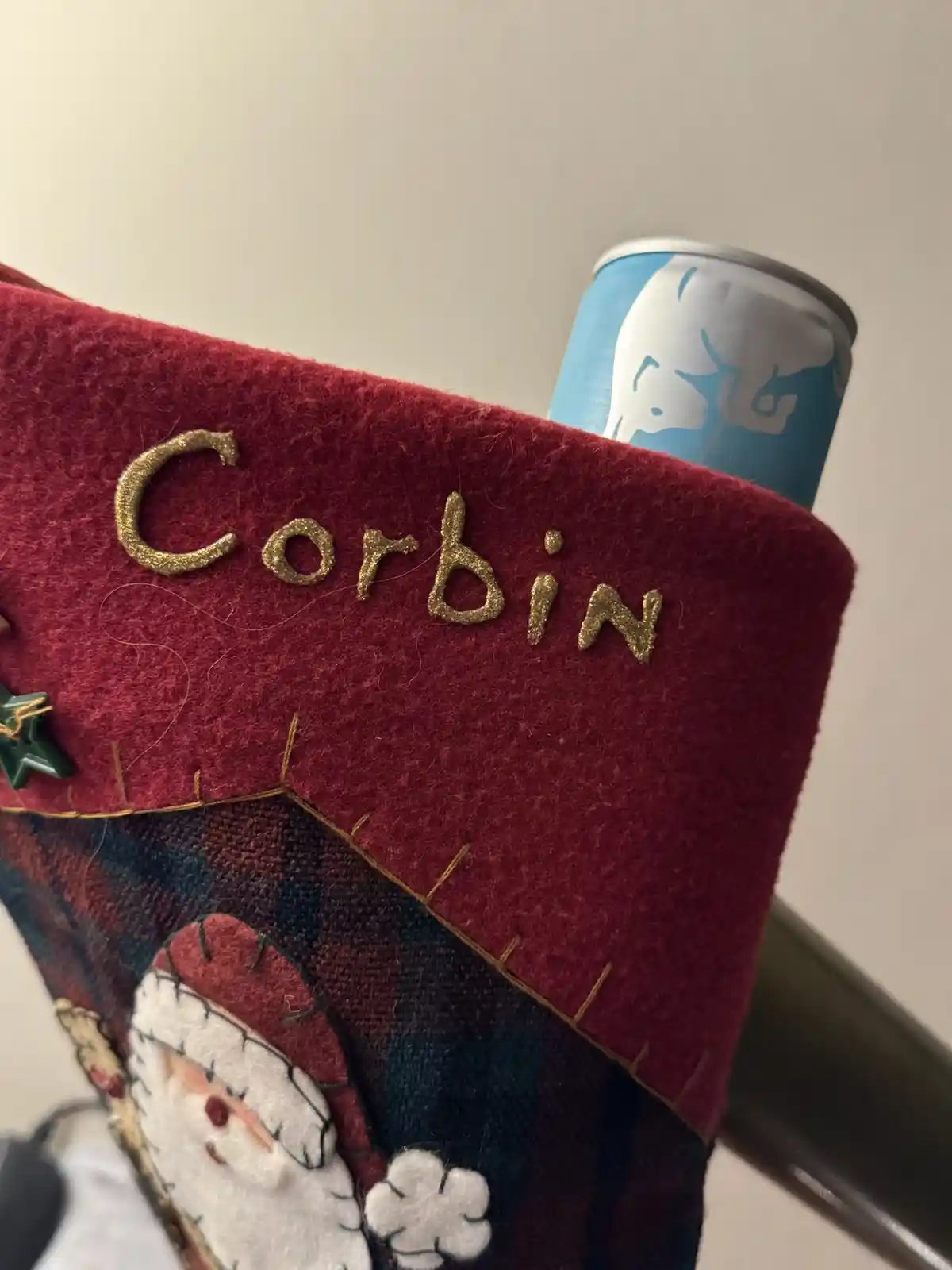 A close-up of a red, handmade Christmas stocking with the name 'Corbin' embroidered in gold glitter letters. The stocking…