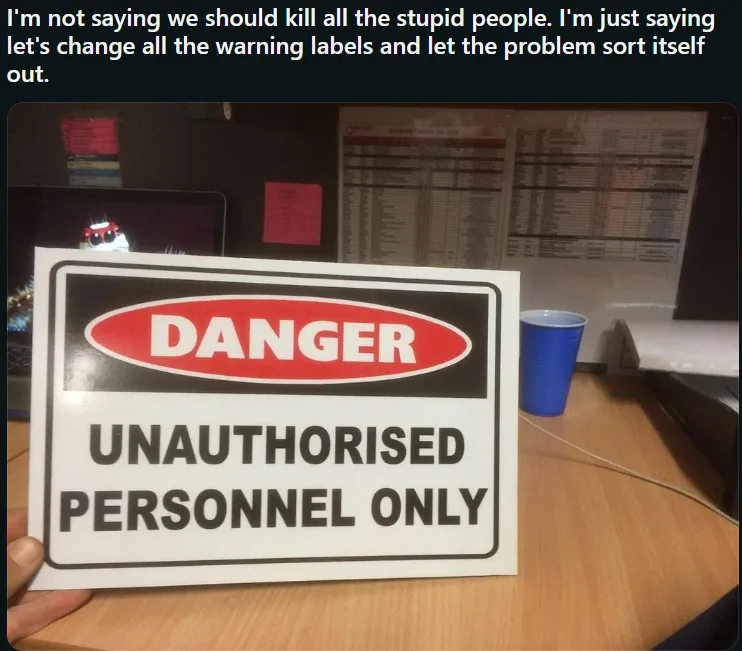 A person holds up a 'DANGER UNAUTHORISED PERSONNEL ONLY' sign in an office setting, with a laptop, blue cup, and charts…
