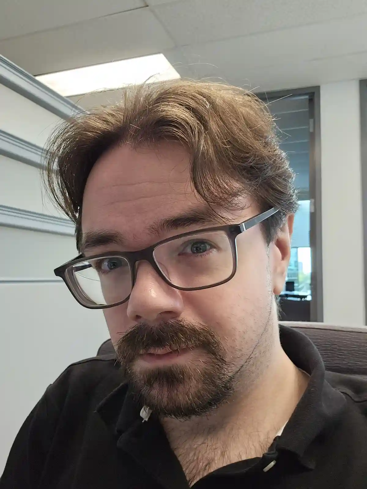A close-up selfie of a man with brown hair, glasses, and a mustache, looking directly at the camera with a slightly weary or…