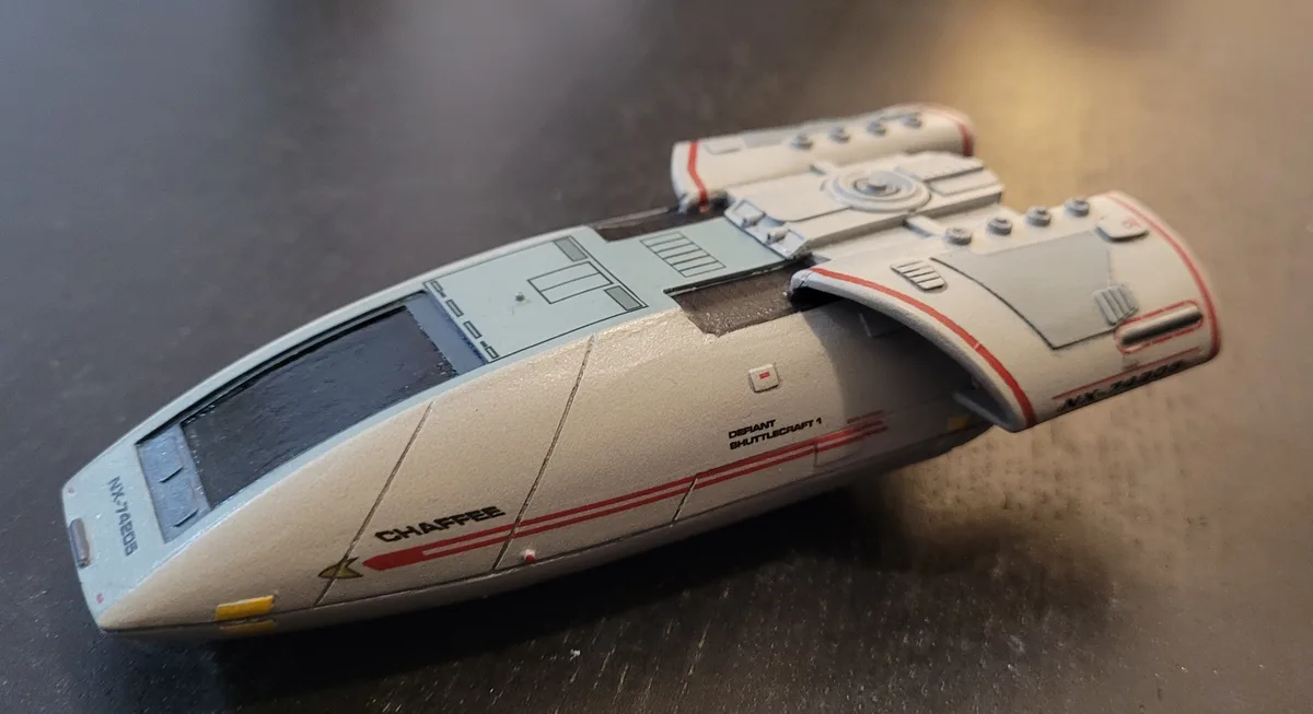A close-up photo of a Star Trek Defiant shuttlecraft model, labeled 'CHAFFEE' and 'DEFIANT SHUTTLECRAFT 1', lying on a dark…