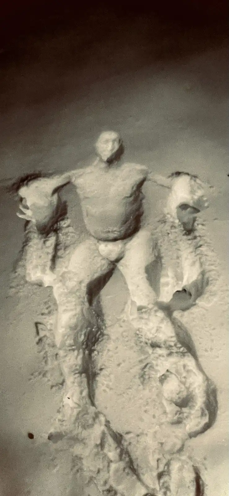 A blurry, sepia-toned image shows a snow sculpture of a man with two smaller snow figures, one on each shoulder, resembling…