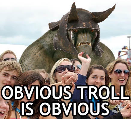 A group of smiling tourists pose for a photo in front of a large, menacing statue of a horned, green-skinned troll. The…