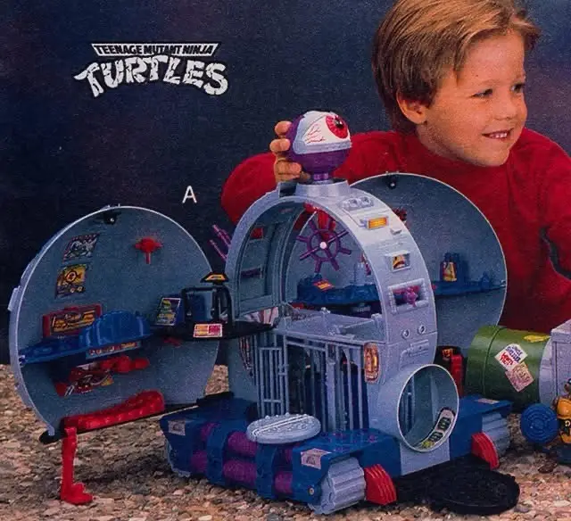 A young boy in a red shirt smiles while holding a purple and white toy dome piece above a large, open blue and purple…