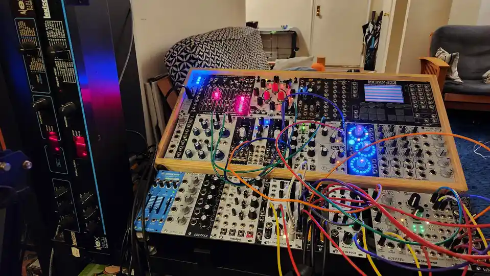 A photo shows a cluttered modular synthesizer setup with multiple Eurorack modules from brands like Doepfer, Tiptop, and…