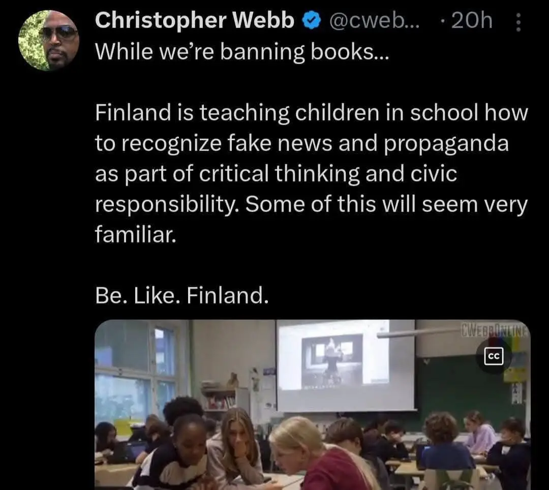 A screenshot of a tweet by Christopher Webb showing a classroom of children seated at desks, watching a presentation on a…
