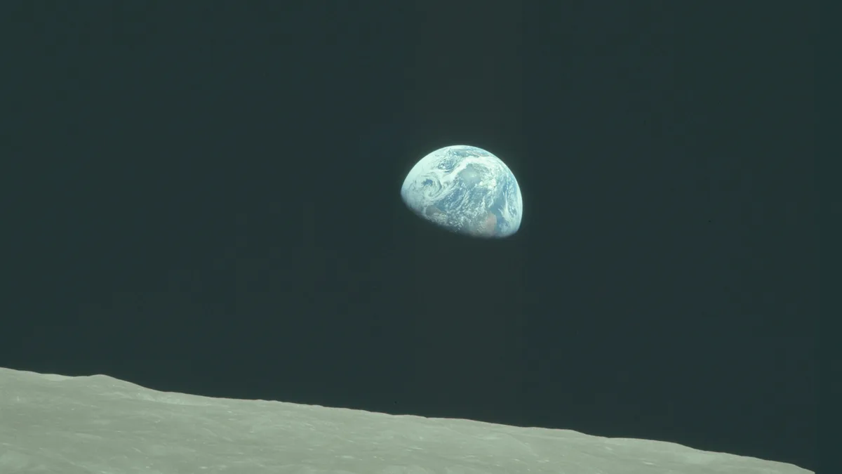 A historic photograph shows the Earth rising above the lunar horizon, with its blue oceans and white clouds visible against…