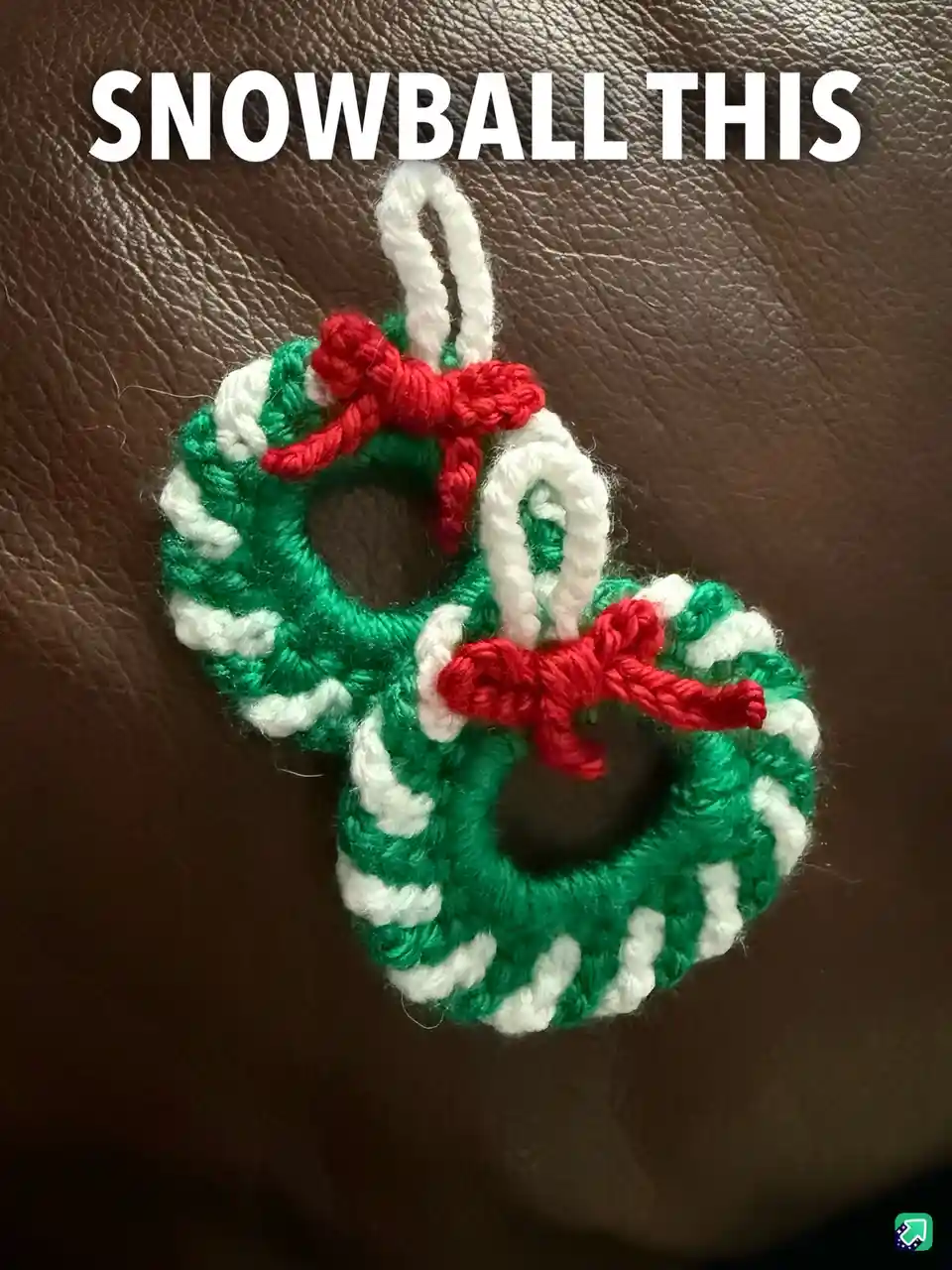 A close-up photo shows two small, crocheted Christmas wreaths made of green and white yarn, each adorned with a red bow and…