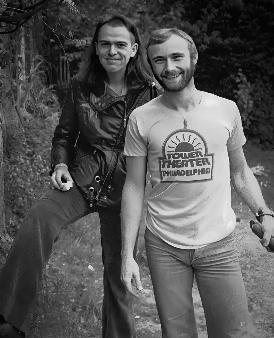 A black-and-white photo shows two smiling men outdoors, one in a leather jacket and the other in a t-shirt with a 'Tower…