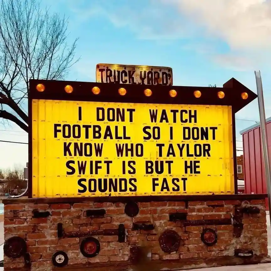 A yellow marquee sign with black lettering reads 'I DONT WATCH FOOTBALL SO I DONT KNOW WHO TAYLOR SWIFT IS BUT HE SOUNDS…