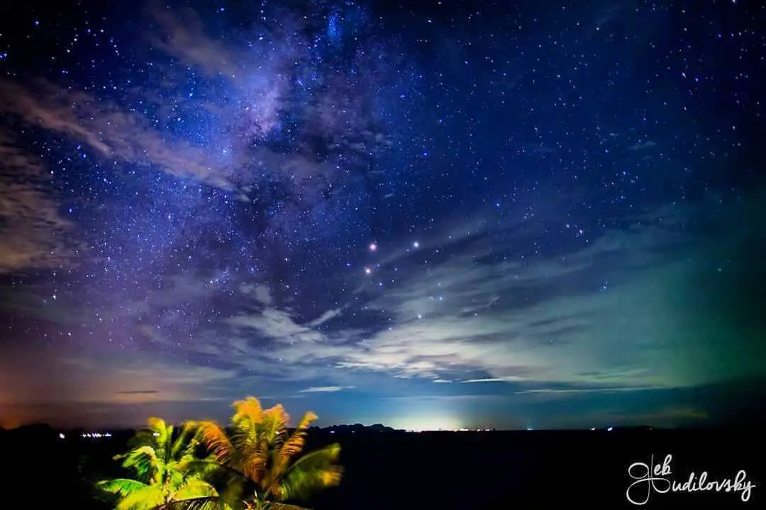 A stunning night sky photograph showing the Milky Way galaxy with countless stars and wispy clouds, above a dark silhouette…