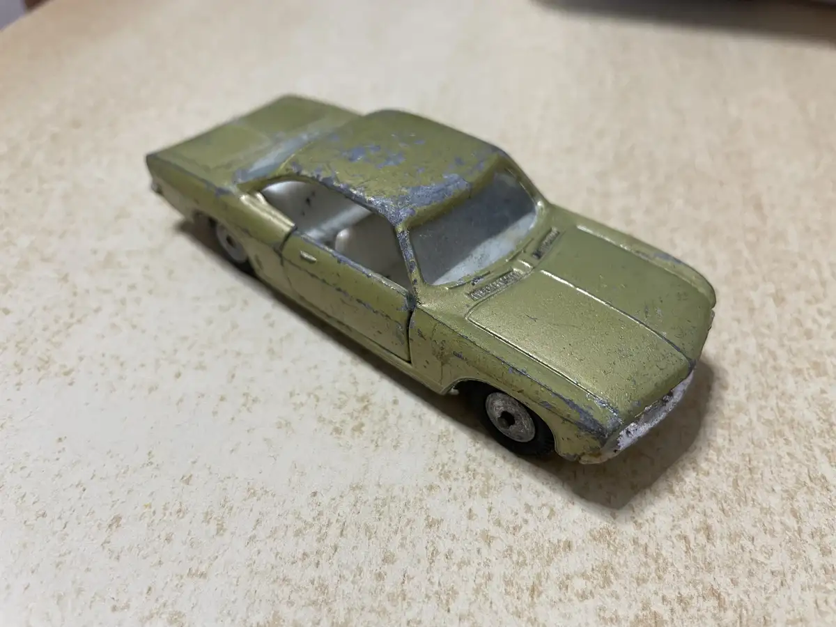 A weathered, olive-green toy car with chipped paint and visible wear sits on a speckled beige countertop. The overlaid text…