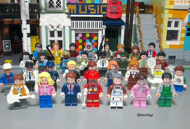 A large group of diverse LEGO minifigures, including musicians, athletes, and various professions, are posed in front of a…