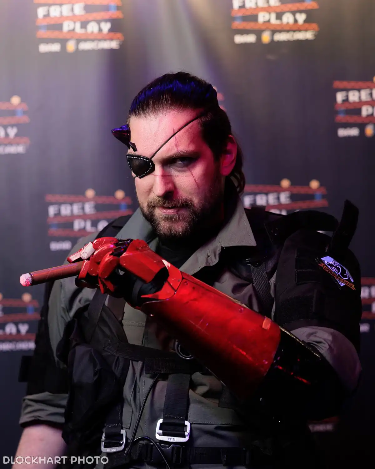 A man in cosplay as a video game character with a red mechanical arm and an eyepatch holds a cigar, standing in front of a…