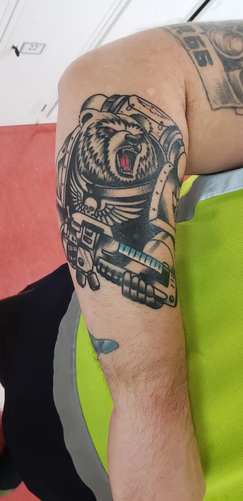 A close-up photo shows a person's tattooed forearm featuring a roaring bear wearing a futuristic helmet and holding a large…