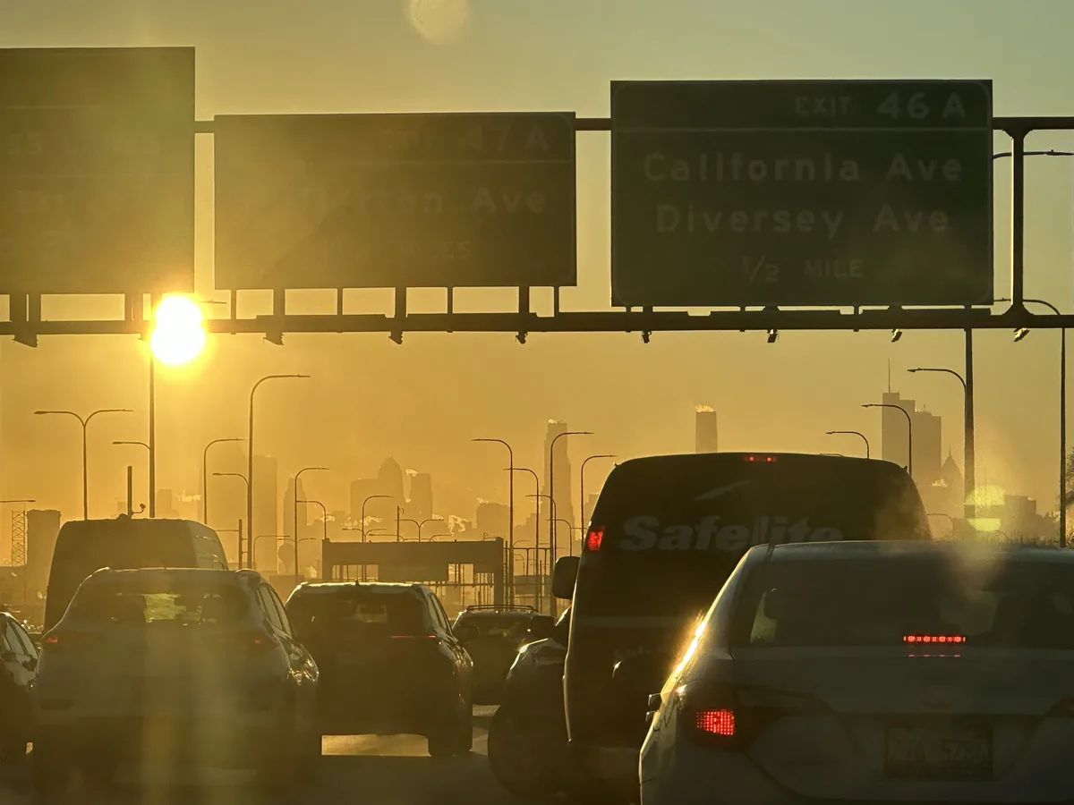 A traffic jam on a highway at sunset, with cars stopped under highway signs that read 'EXIT 46A California Ave Diversey Ave…