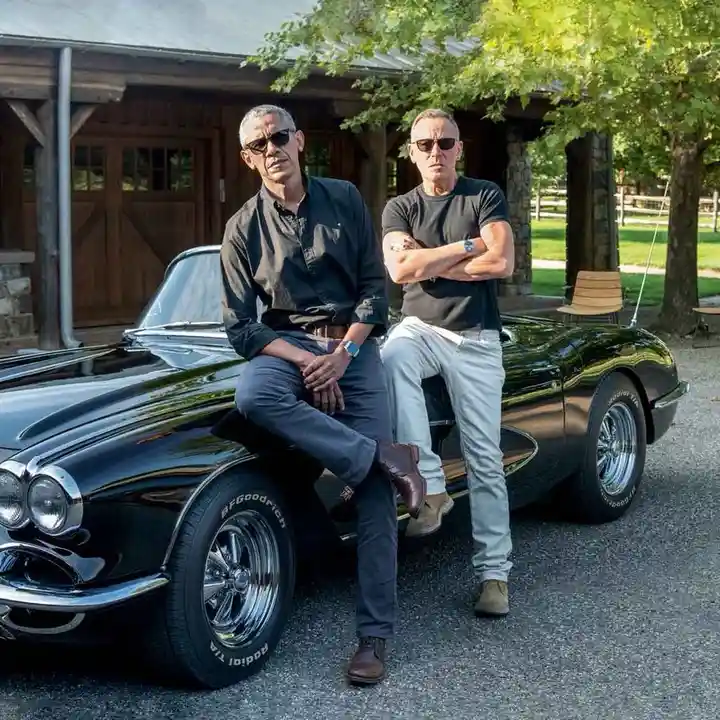 Two men, identified as former U.S. President Barack Obama and actor Daniel Craig, are posing confidently beside a glossy…
