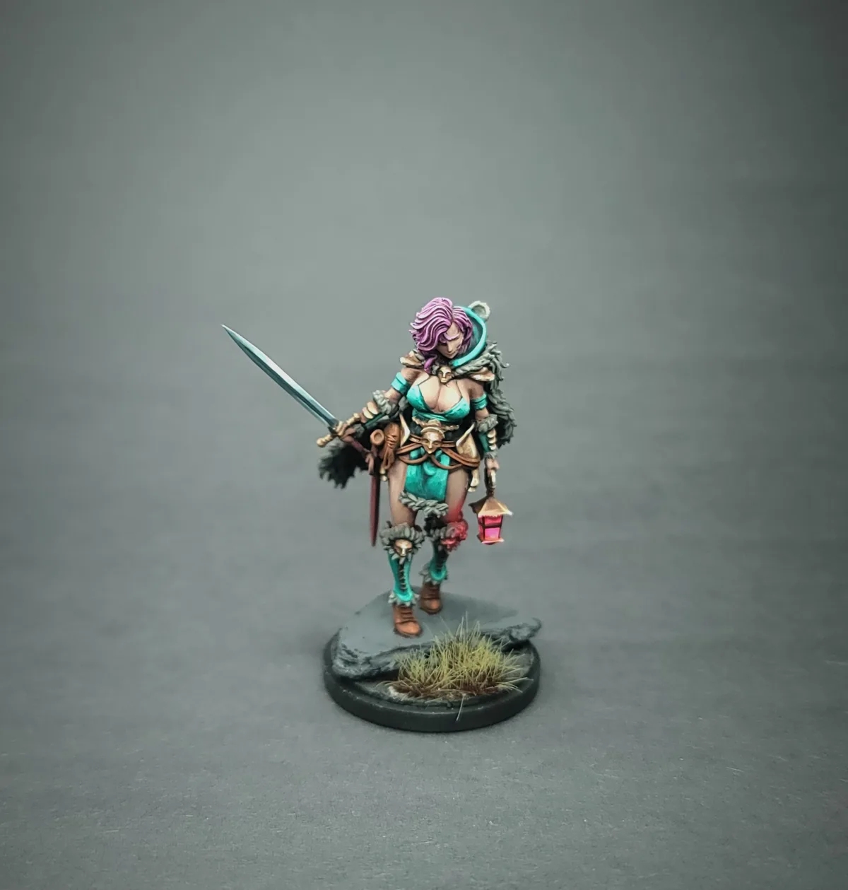 A painted miniature figurine of a female warrior with purple hair, wearing teal armor and fur trim, holding a sword in one…