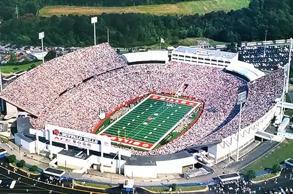 An aerial view of a packed football stadium with a green field and red end zones, surrounded by dense crowds of spectators…