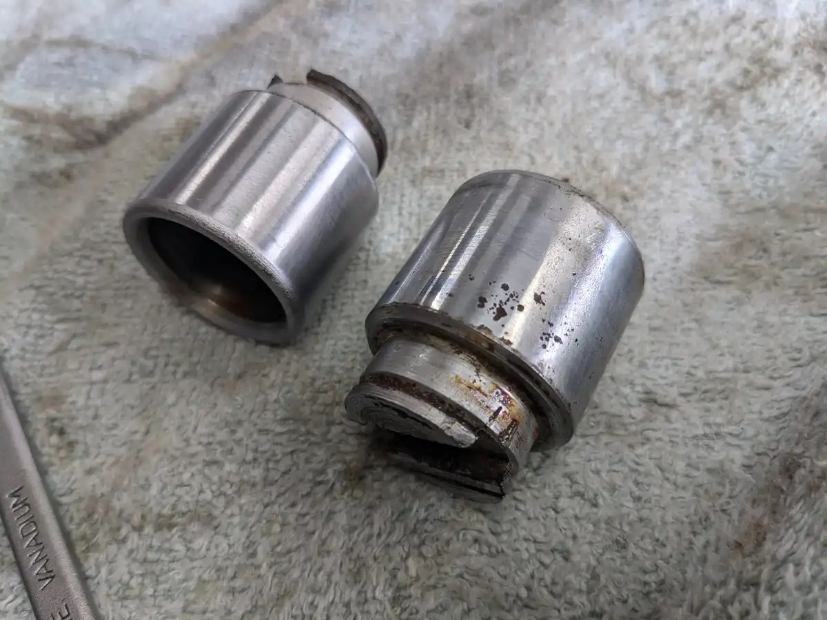 Two worn, dirty metal cylindrical parts lie on a textured gray towel, one showing significant rust and damage at its base. A…