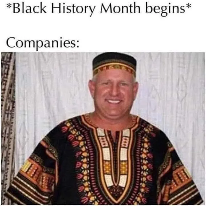 A man with a wide smile wears a colorful African-style dashiki and matching cap against a patterned curtain backdrop. The…