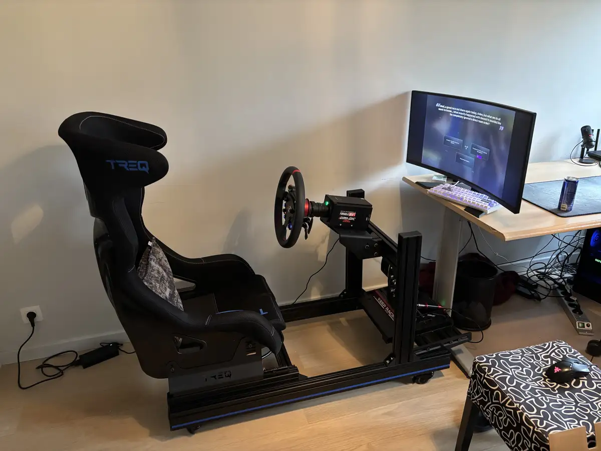 A racing simulator setup with a black TREQ racing seat, a steering wheel mounted on a Simagic racing rig, and a curved…