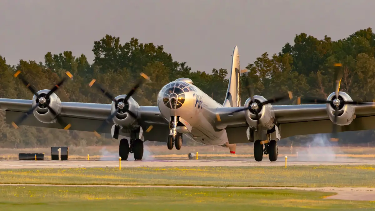 A vintage, silver, four-engine propeller airplane with spinning propellers is captured mid-takeoff or landing on a runway…