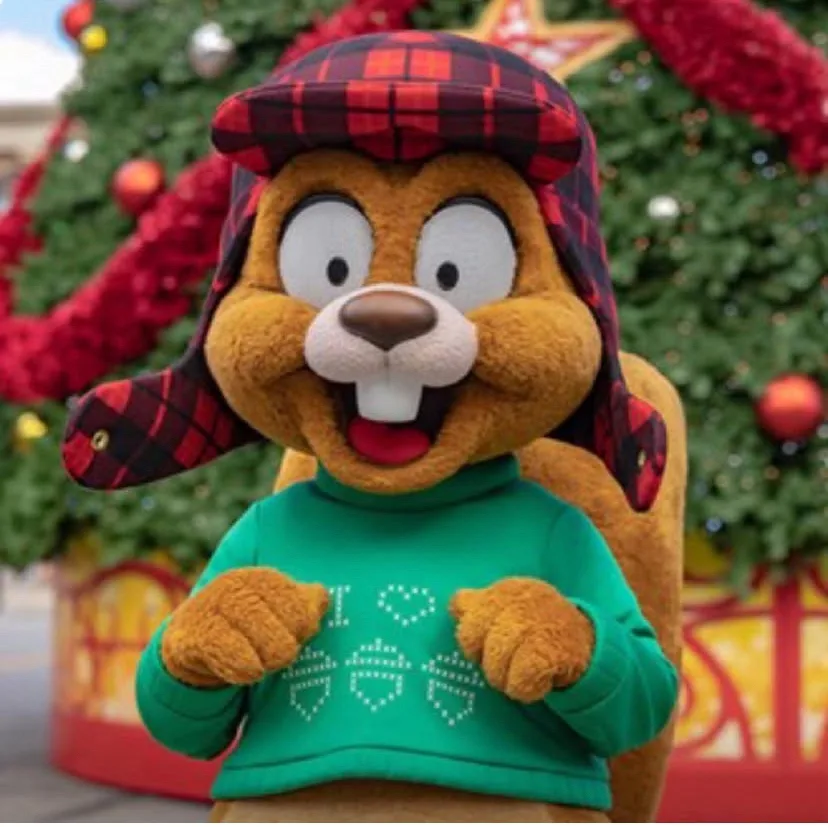 A plush beaver mascot wearing a red and black plaid hat and a green sweater with the text 'I ❤️ 🐿️ 🐿️ 🐿️' knitted on it…