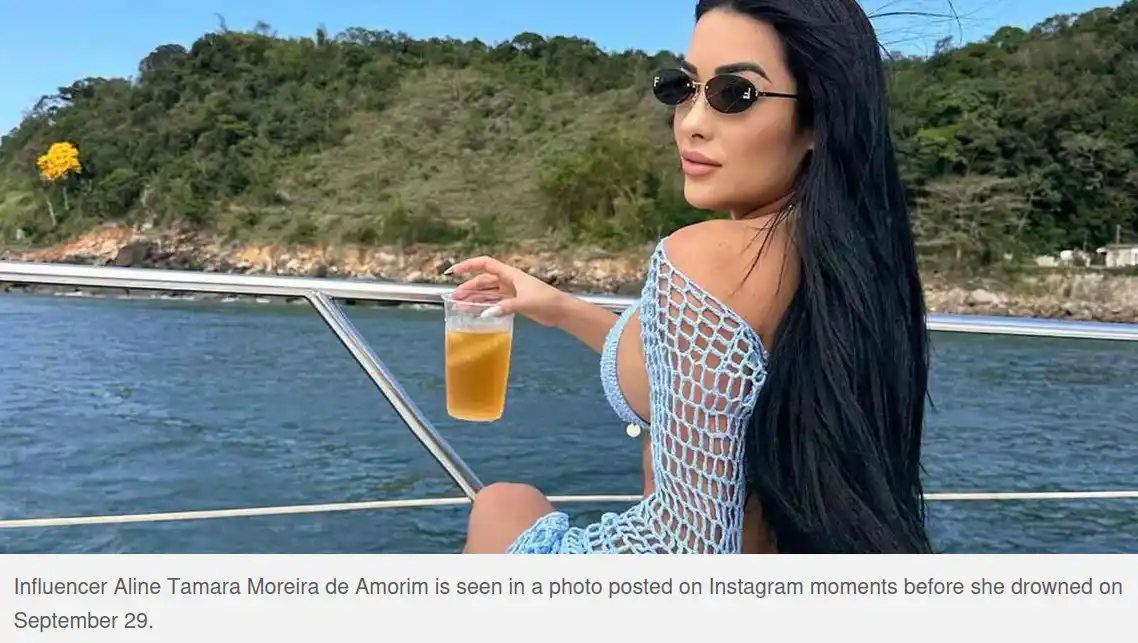 A woman with long black hair and sunglasses sits on a boat, wearing a light blue crochet top and holding a drink. Behind her…