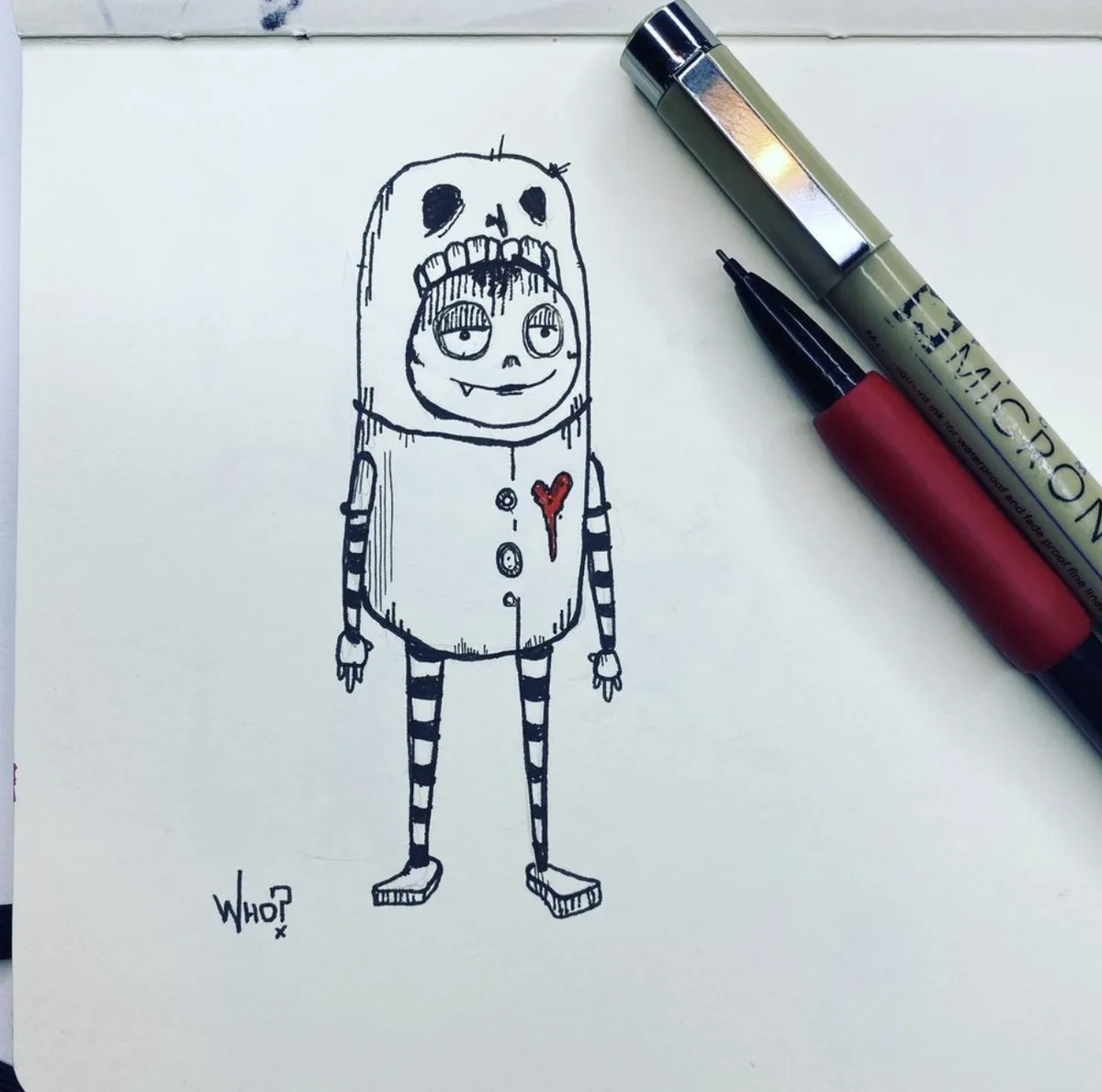 A hand-drawn sketch on white paper shows a cartoonish, skeletal figure wearing a hooded outfit with a stitched mouth and a…