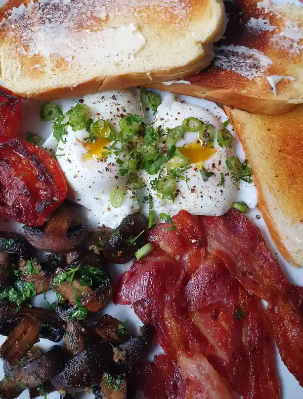 A close-up photo of a hearty breakfast plate featuring two poached eggs with runny yolks, garnished with chopped green…