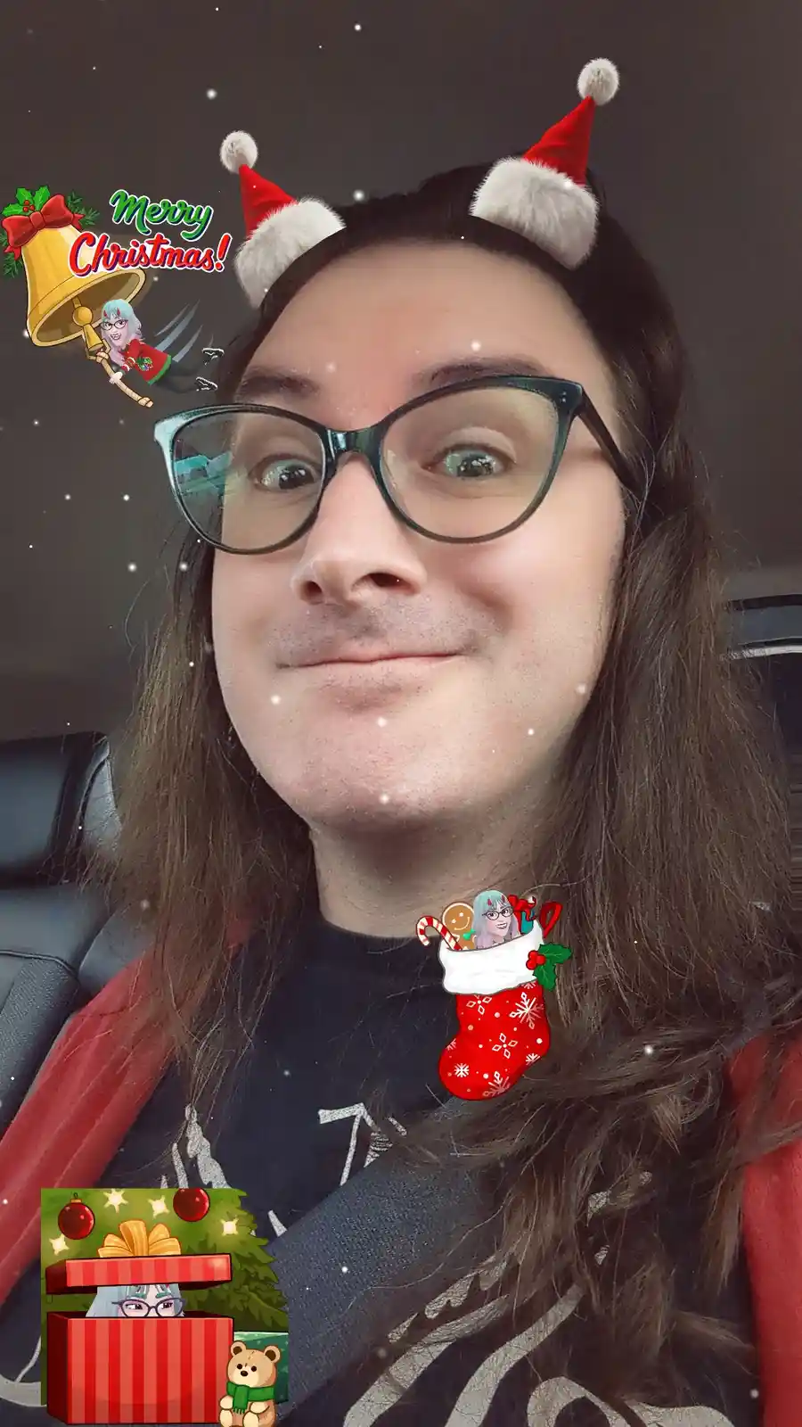 A person with long dark hair and glasses is in a selfie with a festive filter applied. The filter adds cartoonish red Santa…