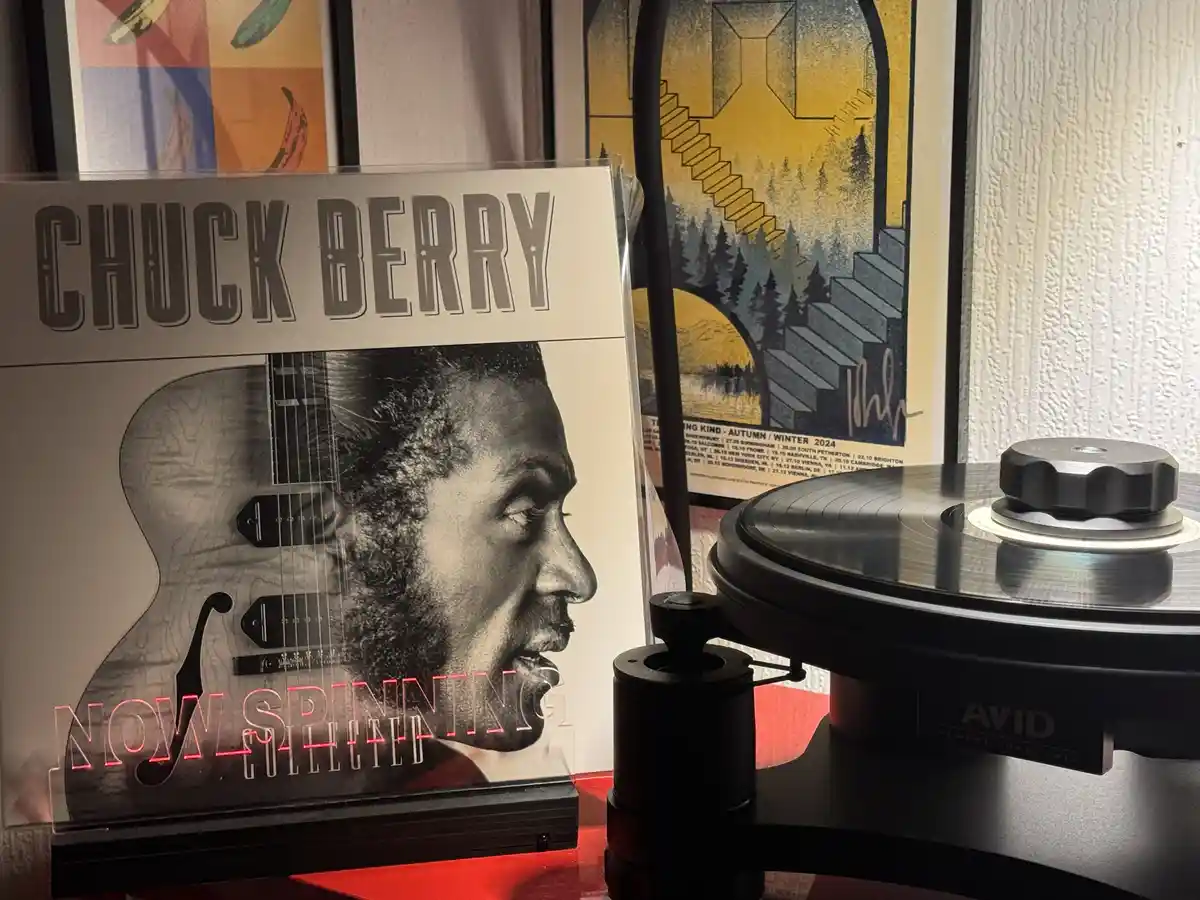 A vinyl record player with a black turntable and tonearm sits next to a Chuck Berry album cover titled 'Now Spinning…