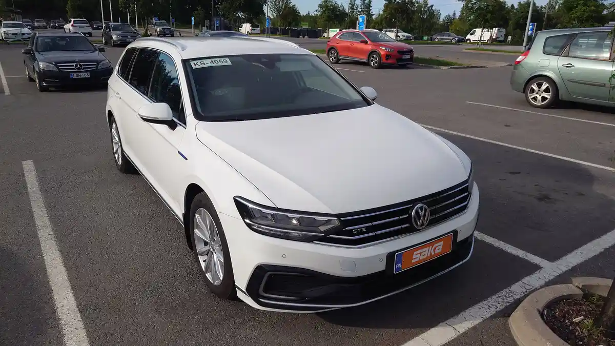 A white Volkswagen Passat GTE station wagon is parked in a lot with other cars, featuring a Finnish license plate that reads…