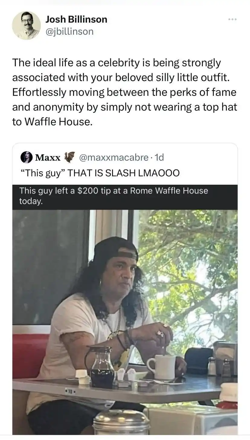 A man with long dark hair and a black baseball cap sits at a diner table, holding a spoon over a white mug. He wears a white…