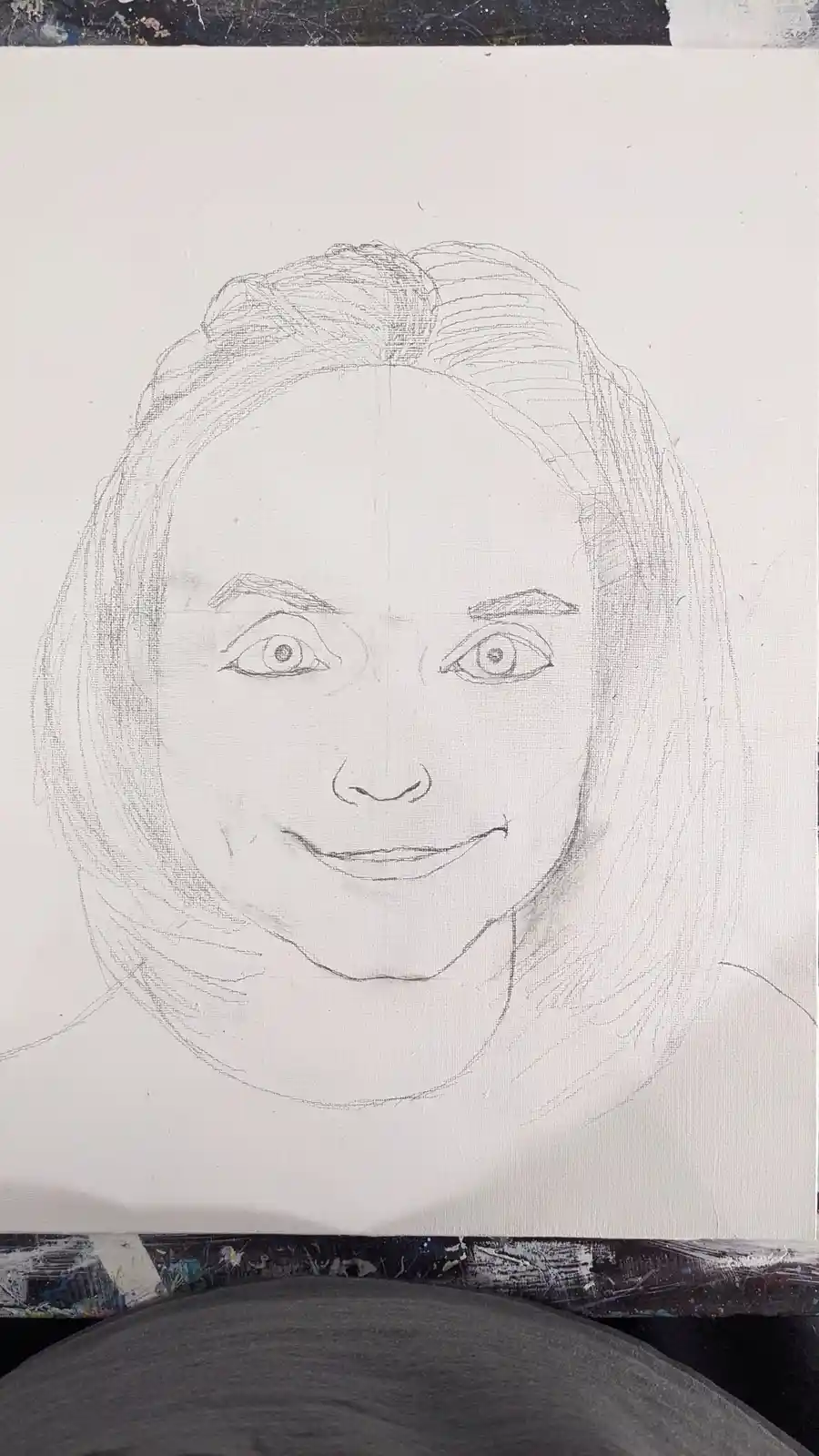 A pencil sketch on canvas shows a person's face with wide, staring eyes and a wide, unnerving smile. The drawing is…