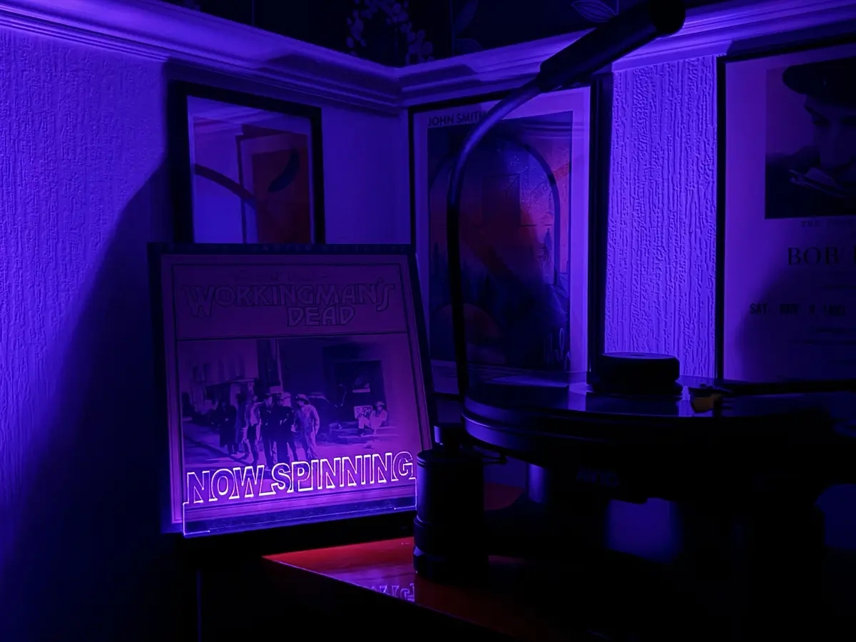 A dimly lit room bathed in purple light features a turntable with a record playing, next to a framed Grateful Dead…