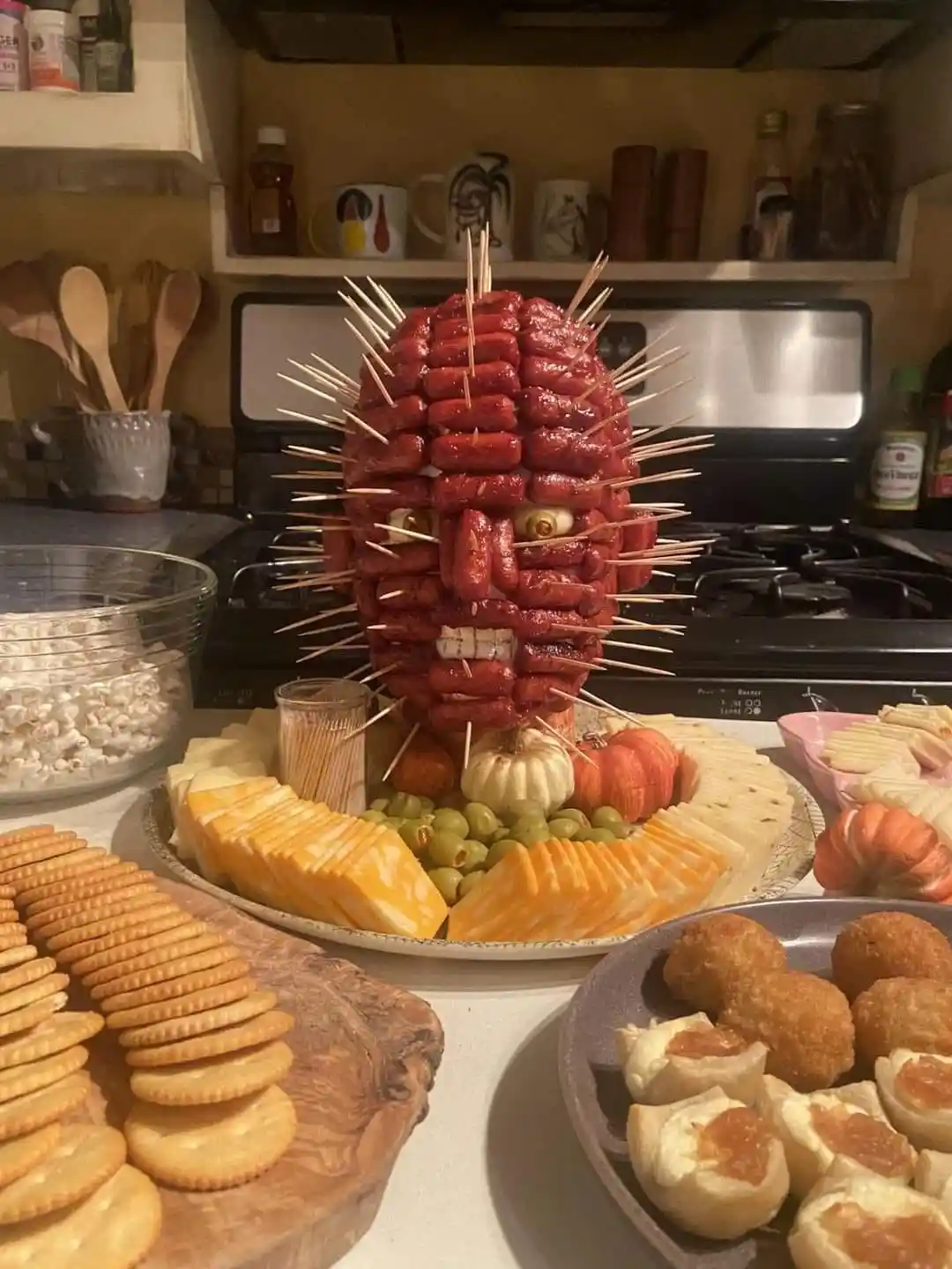 a food platter features a grotesque face sculpture made from grilled hot dogs arranged in a skull-like shape, with…