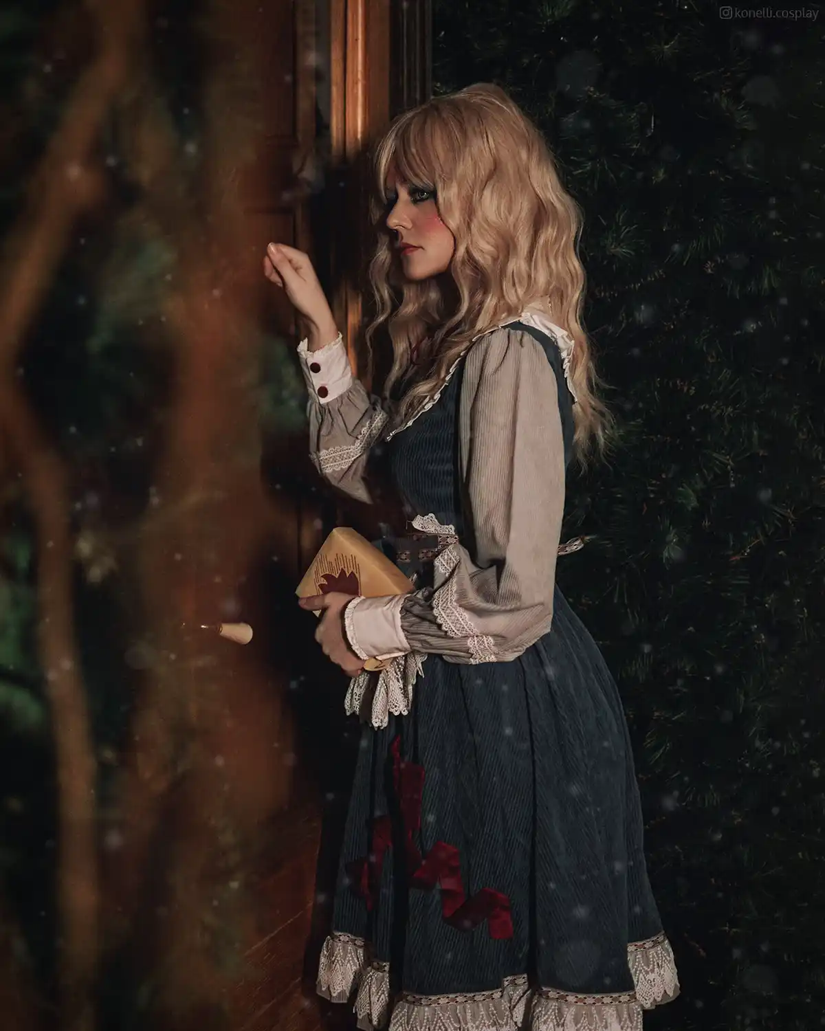 A person in a vintage-style dress with lace cuffs and red ribbon details stands in a snowy, pine-forested setting, holding a…