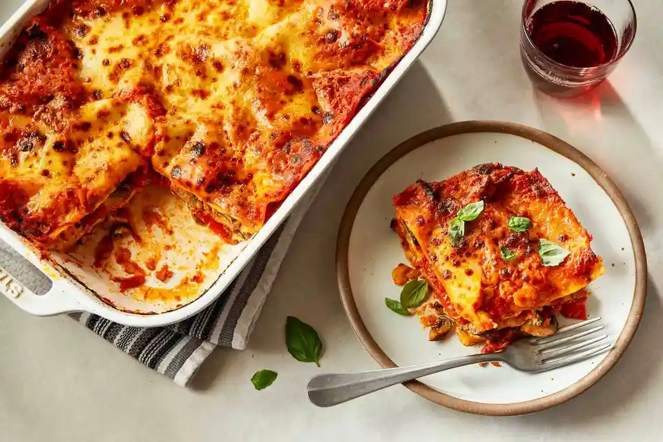 A professionally styled photo shows a white baking dish with a partially eaten lasagna, its golden-brown cheese crust and…