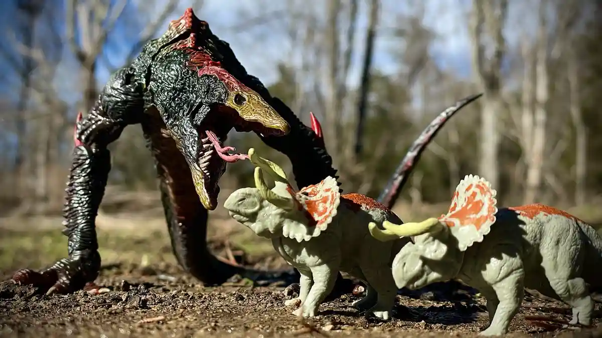 A large, dark green dinosaur toy with red accents and an open mouth is positioned to attack two smaller, light green…