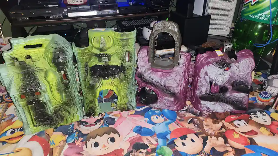 Four large, colorful plastic castle-shaped toy boxes are arranged on a blanket featuring various video game characters. Two…
