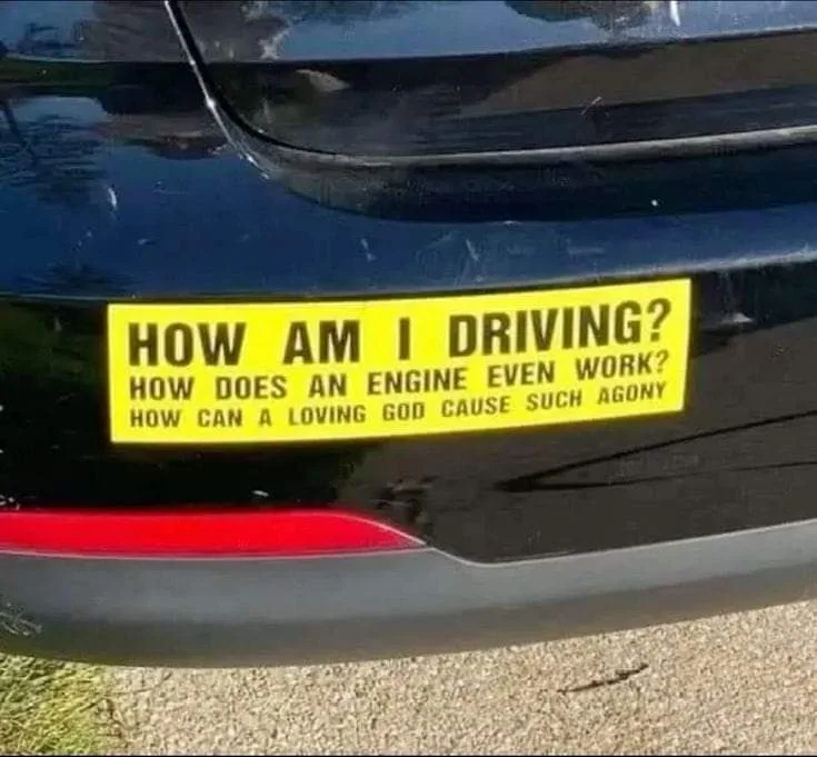 A close-up of the rear of a black car showing a bright yellow bumper sticker with three lines of black text. The text reads…