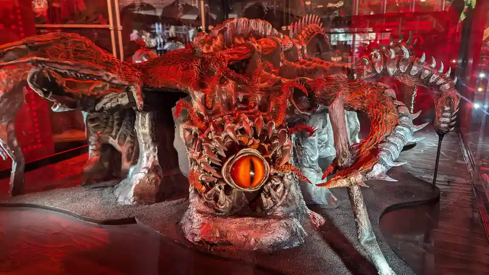 A large, menacing demonic sculpture with multiple spiky limbs, glowing orange eyes, and a wide mouth full of sharp teeth is…