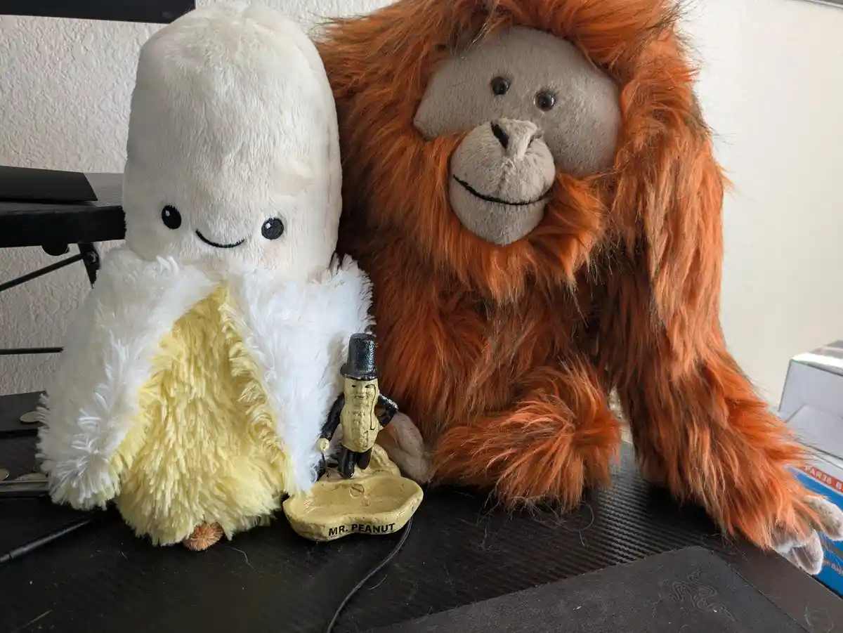 A plush banana character with a white top and yellow bottom sits next to a large orange-furred stuffed orangutan, with a…