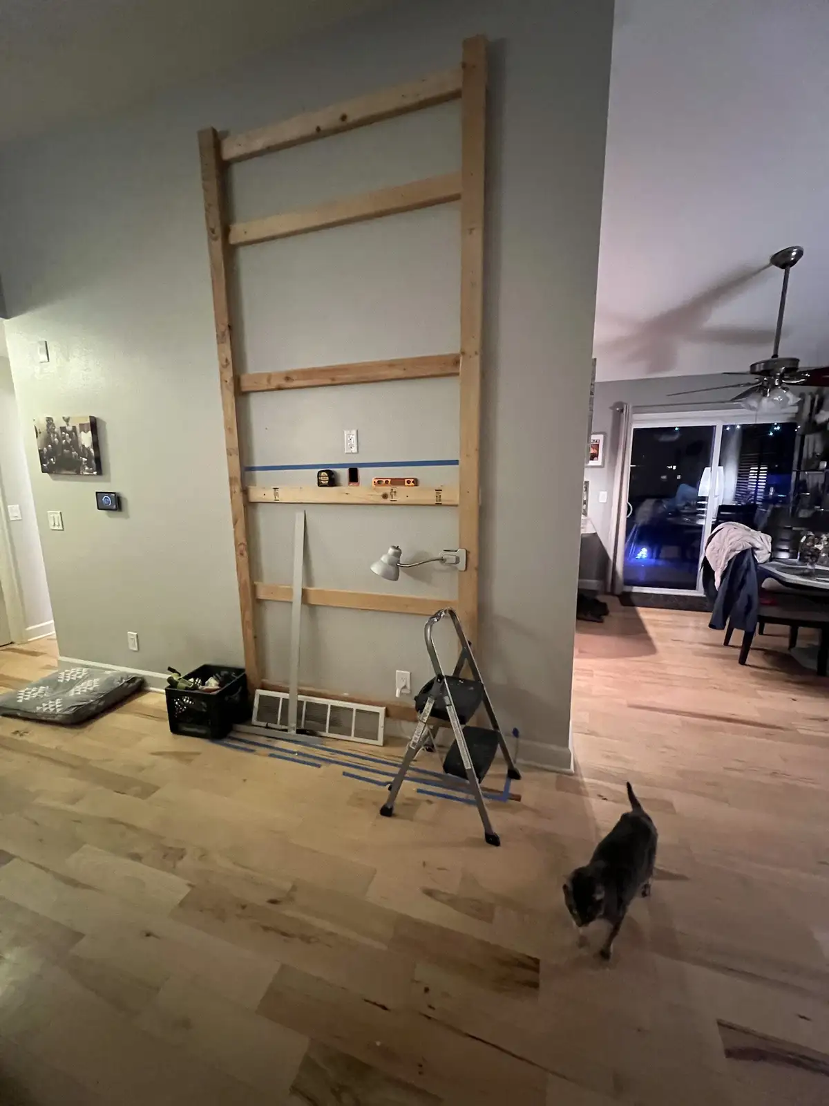 A wooden ladder structure is mounted vertically on a light gray wall in a home, with tools and blue painter's tape on the…