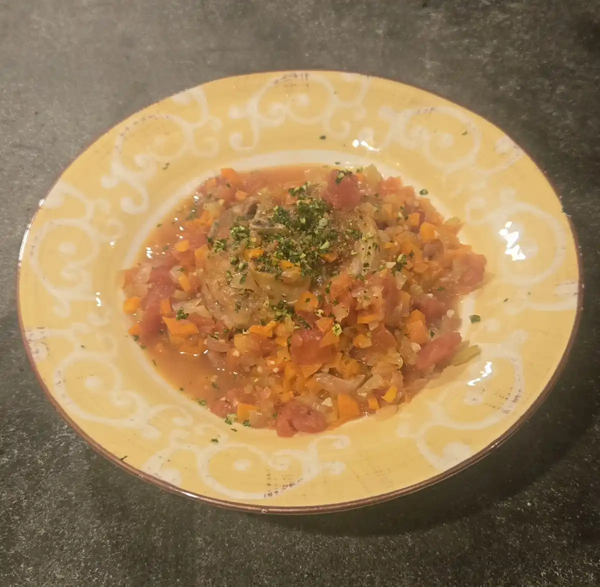 A close-up photo shows a yellow plate with a white scroll pattern, holding a stew-like dish with chunks of meat, diced…