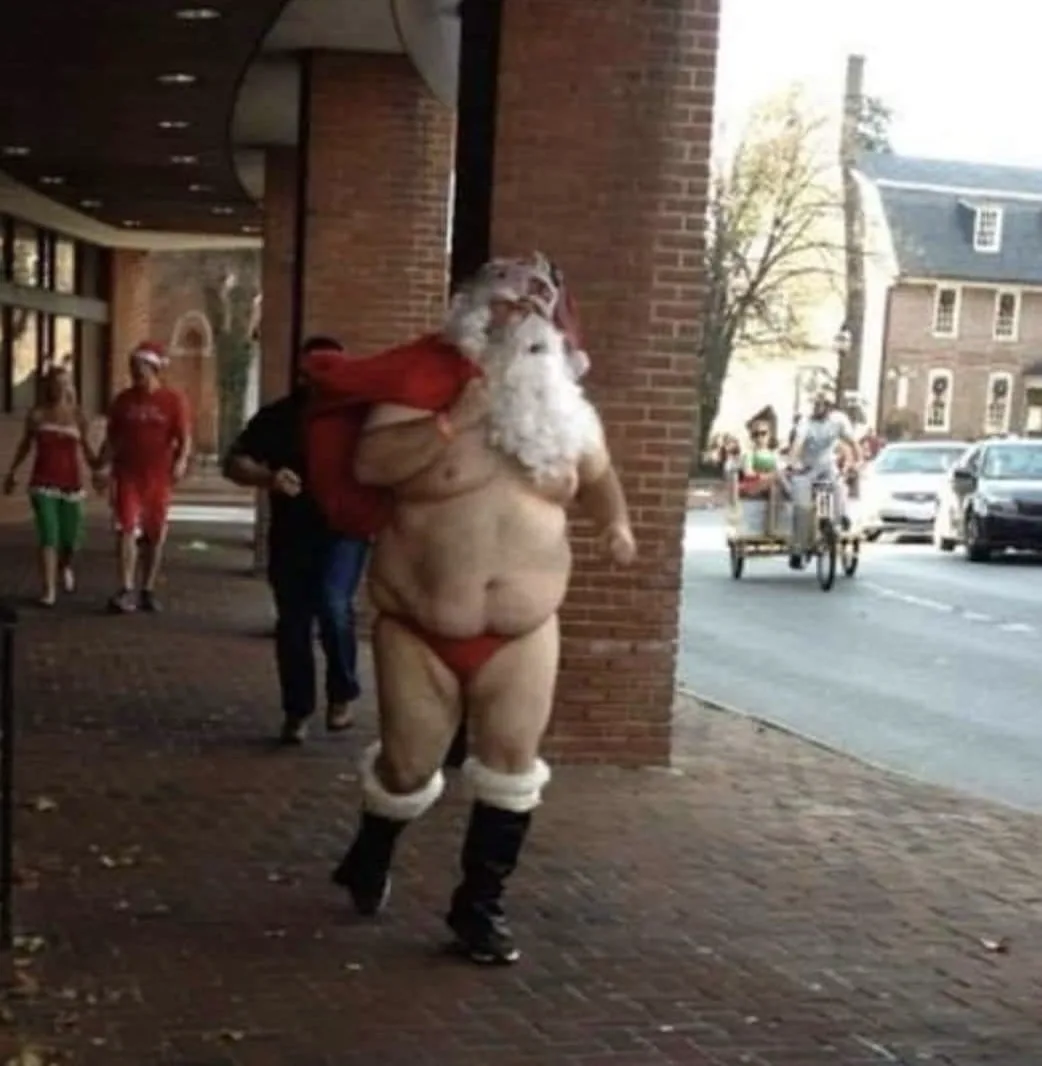 A man dressed as Santa Claus, wearing only red underwear, boots, and a Santa hat, carries a red sack while walking on a…